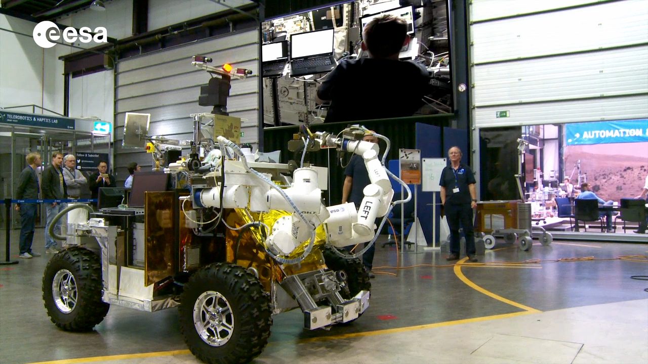 A robotic vehicle with a robotic arm is displayed in a technology facility.